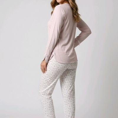 Mulher com pijama rosa claro e calças brancas com padrão floral, de pé em fundo branco