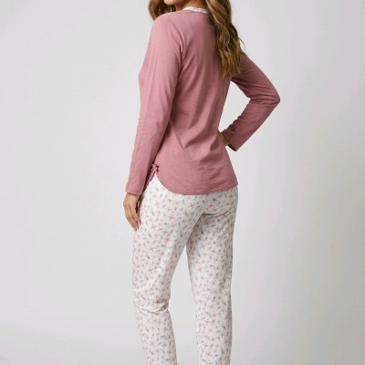 Mulher de costas a usar pijama rosa de manga comprida e calças brancas com padrão floral e sandálias cinzentas.