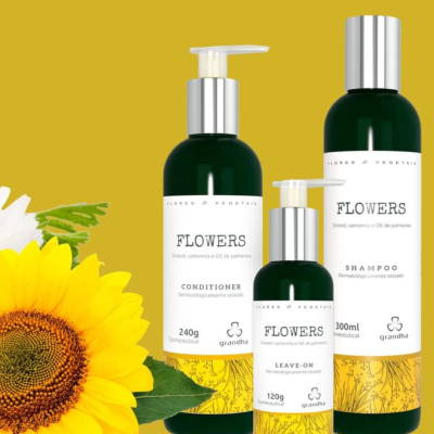 Três frascos verdes de produtos para cabelo da marca Grandha com rótulos brancos e texto em português e inglês, fundo amarelo e flor amarela.