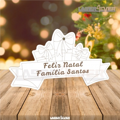 Placa decorativa branca com texto Feliz Natal Família Santos sobre mesa de madeira
