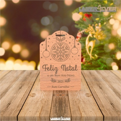 Placa decorativa de madeira gravada com mensagem de Natal e Ano Novo numa mesa de madeira com decoração natalícia ao fundo
