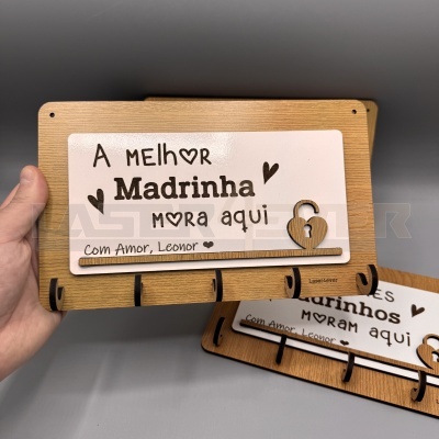 Placa decorativa de madeira para chaves com texto 'A melhor Madrinha mora aqui' e decoração de cadeado