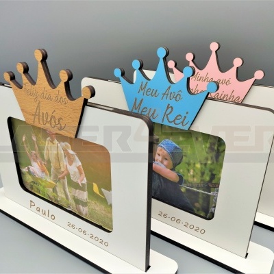 Três molduras de fotografia em madeira com coroas coloridas e gravações, cada uma mostra uma foto ou está vazia.