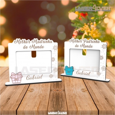 Dois porta-retratos brancos decorados para madrinha e padrinho com nomes, em mesa de madeira com fundo natalício desfocado.