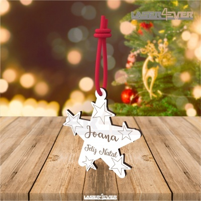Ornamento de Natal branco com estrelas e texto, pendurado por cordão vermelho, com árvore de Natal em fundo desfocado