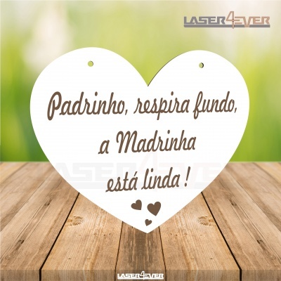 Placa decorativa em forma de coração com texto em português e pequenos corações, sobre madeira e fundo verde desfocado.