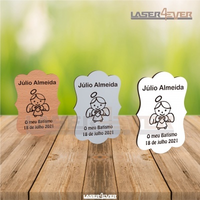 Três placas decorativas para batismo em diferentes materiais sobre mesa de madeira