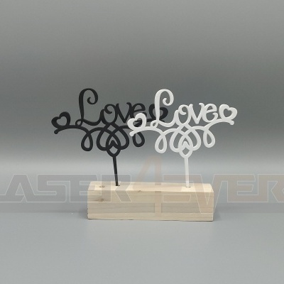 Dois objectos decorativos com a palavra 'Love' em acrílico, um preto e um branco, sobre base de madeira.
