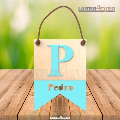 Plaquinha de madeira com a letra P azul e nome Pedro recortado, pendurada por corda, sobre mesa de madeira.