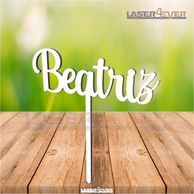 Topper branco em forma do nome Beatriz sobre mesa de madeira com fundo verde desfocado