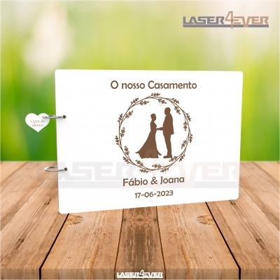 Livro de memórias branco com silhueta de casal de noivos e texto em castanho sobre uma mesa de madeira