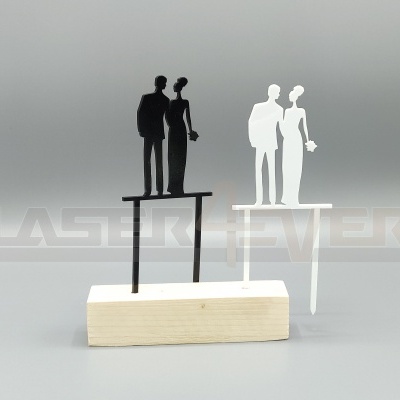 Toppers de bolo em formato de casal de noivos, um preto e outro branco, com base em madeira clara.