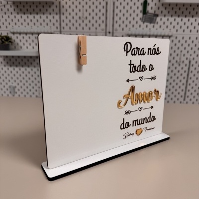 Placa decorativa branca com texto em preto e dourado numa base preta e pregador de madeira