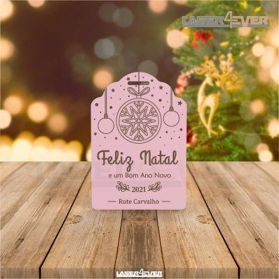 Cartão de Natal rosa com texto e desenhos de bolas de Natal em mesa de madeira