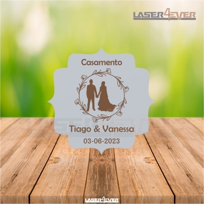 Etiqueta branca com desenho de casal e texto de casamento sobre fundo verde e madeira