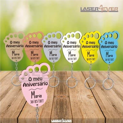 Sete chaveiros coloridos em forma de pé com texto comemorativo, sobre mesa de madeira