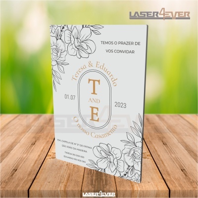 Convite de casamento branco com flores a preto e texto em português sobre fundo de madeira