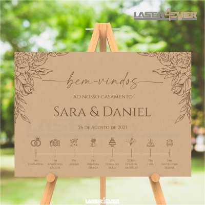Placa de casamento com texto em castanho sobre papel castanho, decorada com flores, em cavalete de madeira ao ar livre