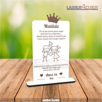 Quadro decorativo em madeira com texto em português e desenho de duas crianças, numa mesa de madeira com fundo verde