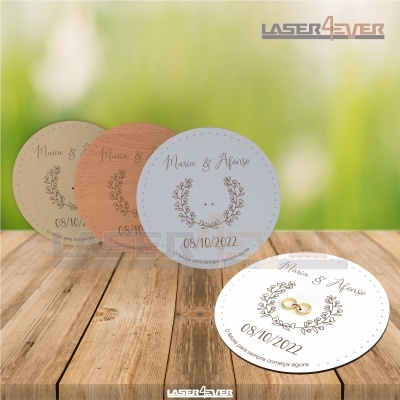 Placas redondas gravadas a laser com nomes Maria & Nuno e data 08/10/2022, com decoração floral e anéis dourados sobre fundo de madeira