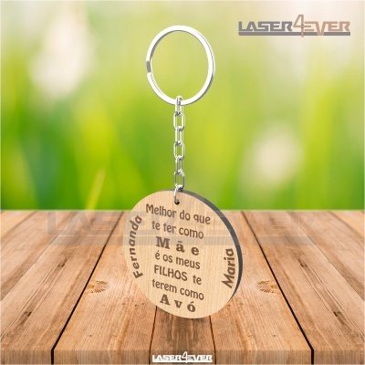 Chaveiro redondo de madeira gravado a laser com texto e nomes, pendurado sobre superfície de madeira clara