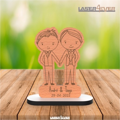 Escultura de madeira com figuras de dois homens e gravação de nomes e data sobre base em fundo verde desfocado.