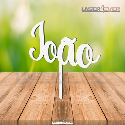 Letreiro branco recortado com a palavra João sobre mesa de madeira