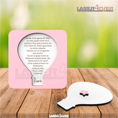 Convite formato balão de fala branco com base rosa e texto, sobre superfície de madeira clara