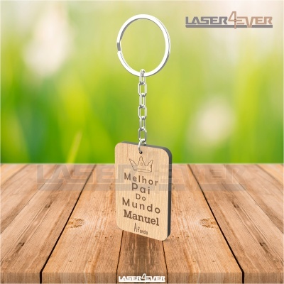 Porta-chaves de madeira gravado com texto em português sobre pai, com corrente de metal prateado, sobre mesa de madeira.