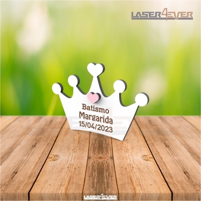Decoração em formato de coroa branca com texto de batismo sobre mesa de madeira