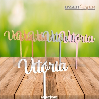 Cinco toppers de bolo com nome 'Vitória' em várias cores sobre mesa de madeira