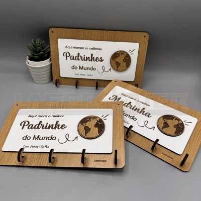 Placas decorativas em madeira com texto em português e globo terrestre, com ganchos pretos, sobre fundo cinzento e planta pequena em vaso branco