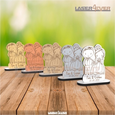 Figuras de noivos em madeira com base negra e texto gravado, em vários tons, sobre mesa de madeira.