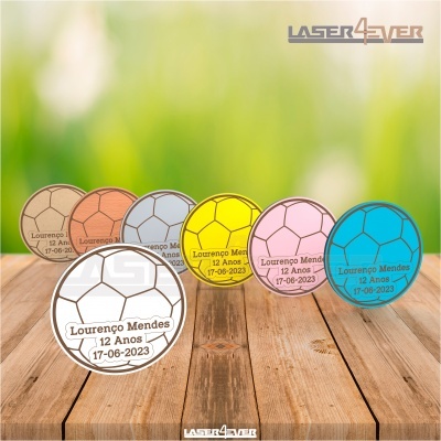 Medalhas coloridas em forma de bola de futebol com texto personalizado sobre mesa de madeira
