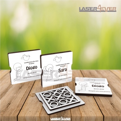 Peças quadradas brancas com ilustrações e texto em português sobre nome e datas junto com jogo da velha prateado em mesa de madeira