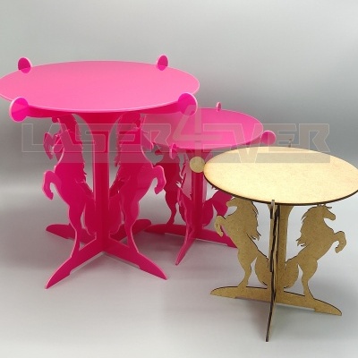 Três mesas redondas de MDF com bases em forma de cavalos, duas rosas e uma madeira natural.