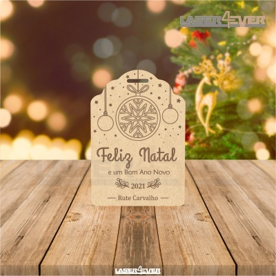 Placa decorativa de madeira com mensagem de Natal e Ano Novo sobre mesa de madeira com decoração festiva ao fundo