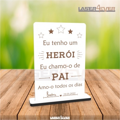 Placa decorativa acrílica branca com texto em castanho sobre base preta e fundo verde desfocado