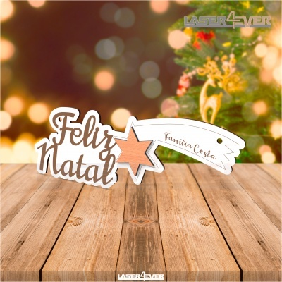 Placa decorativa de madeira com mensagem de Feliz Natal e nome de família, cenário natalício desfocado