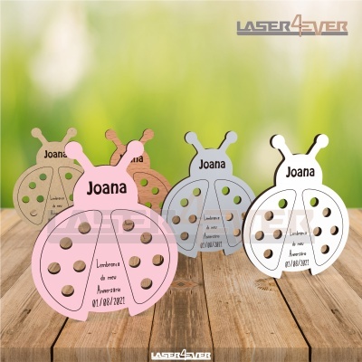 Lembranças de aniversário em forma de joaninhas coloridas com texto gravado, dispostas sobre mesa de madeira.