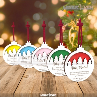 Etiquetas decorativas de Natal coloridas com cordões vermelhos, texto 'Feliz Natal' e mensagem em português, sobre tampo de madeira com fundo natalício iluminado