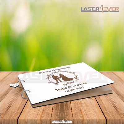 Livro de casamento branco com argolas e pendente de coração, com texto e desenho de casal na capa