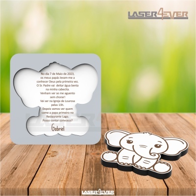 Convite de batizado em forma de elefante com texto em português, sobre mesa de madeira e fundo verde desfocado