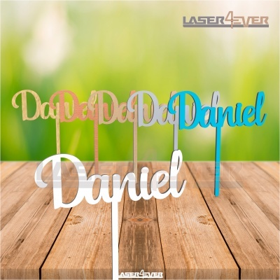 Toppers de bolo com o nome 'Daniel' em várias cores sobre uma mesa de madeira