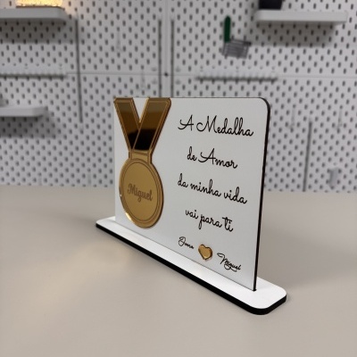 Placa decorativa branca com medalha dourada e texto em português