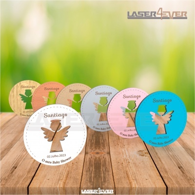 Discos decorativos coloridos com anjos recortados e texto para Baby Shower colocados em superfície de madeira.