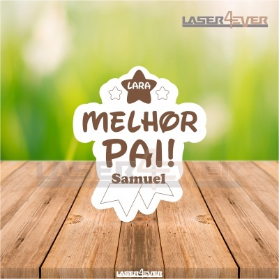 Emblema decorativo branco com texto castanho 'LARA MELHOR PAI! Samuel' sobre madeira com fundo verde desfocado