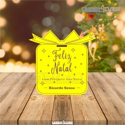 Placa amarela com texto de Natal sobre mesa de madeira e fundo decorativo natalício