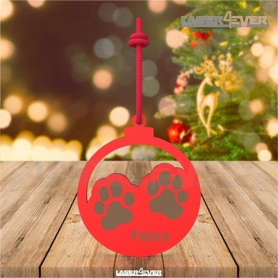 Ornamento de Natal vermelho com pegadas cinzentas e nome 'Faísca', com árvore de Natal ao fundo
