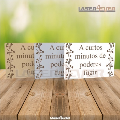 Placas decorativas retangulares com frase e moldura de folhas em três cores sobre mesa de madeira.